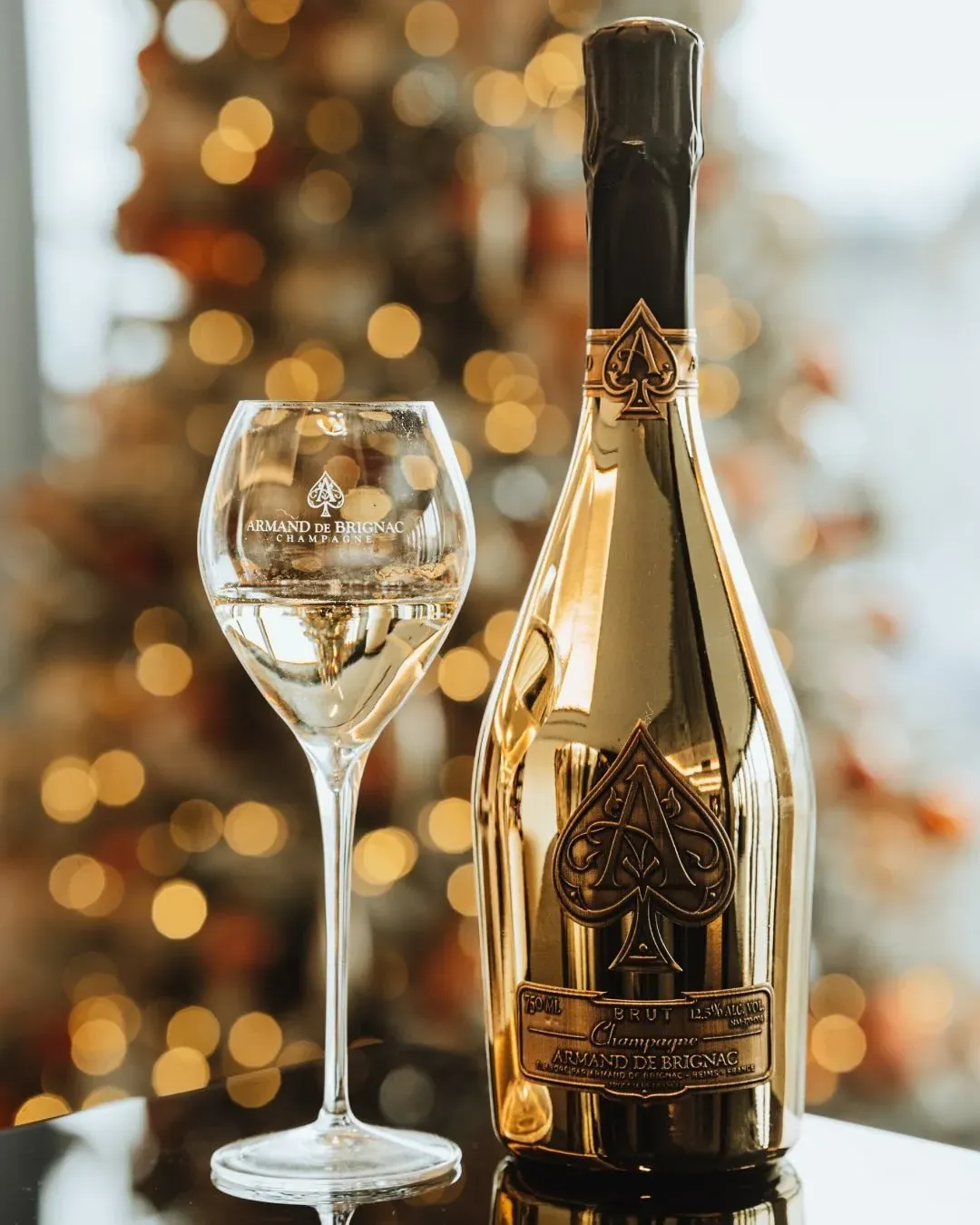 Photographie réelle : bouteille de champagne Armand de Brignac Brut Gold et sa coupe, posées sur une surface sombre